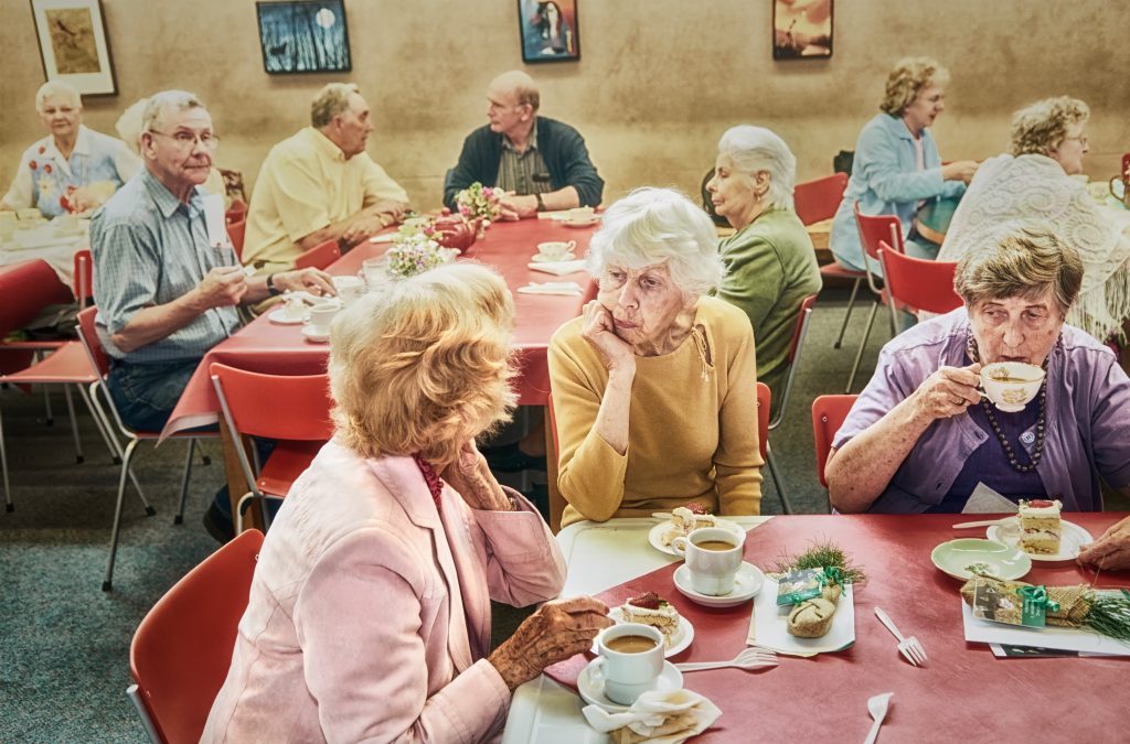 Photo of retirement home residents at a tea party. The interest of the photo is for the way 10 people pictured are relating to each other, attentively, longingly, indifferently, suspiciously...